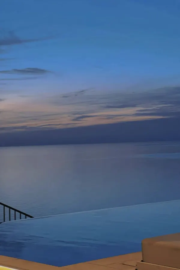 An infinity pool meeting the sea at blue hour.