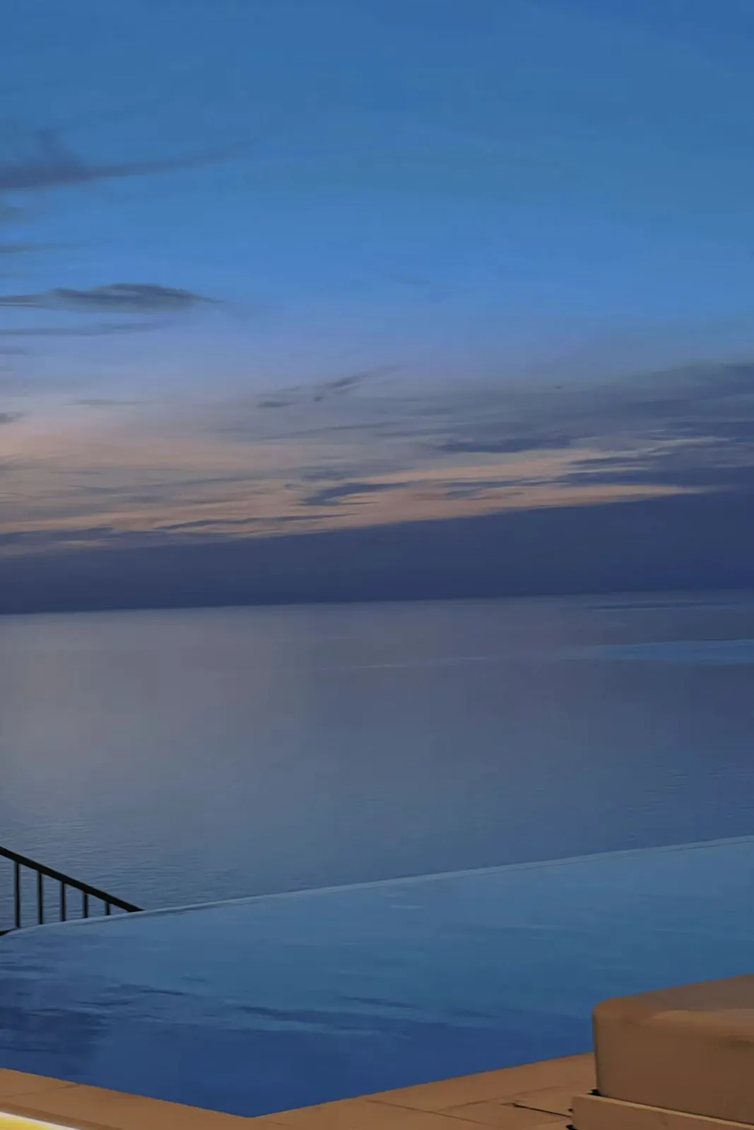 An infinity pool meeting the sea at blue hour.