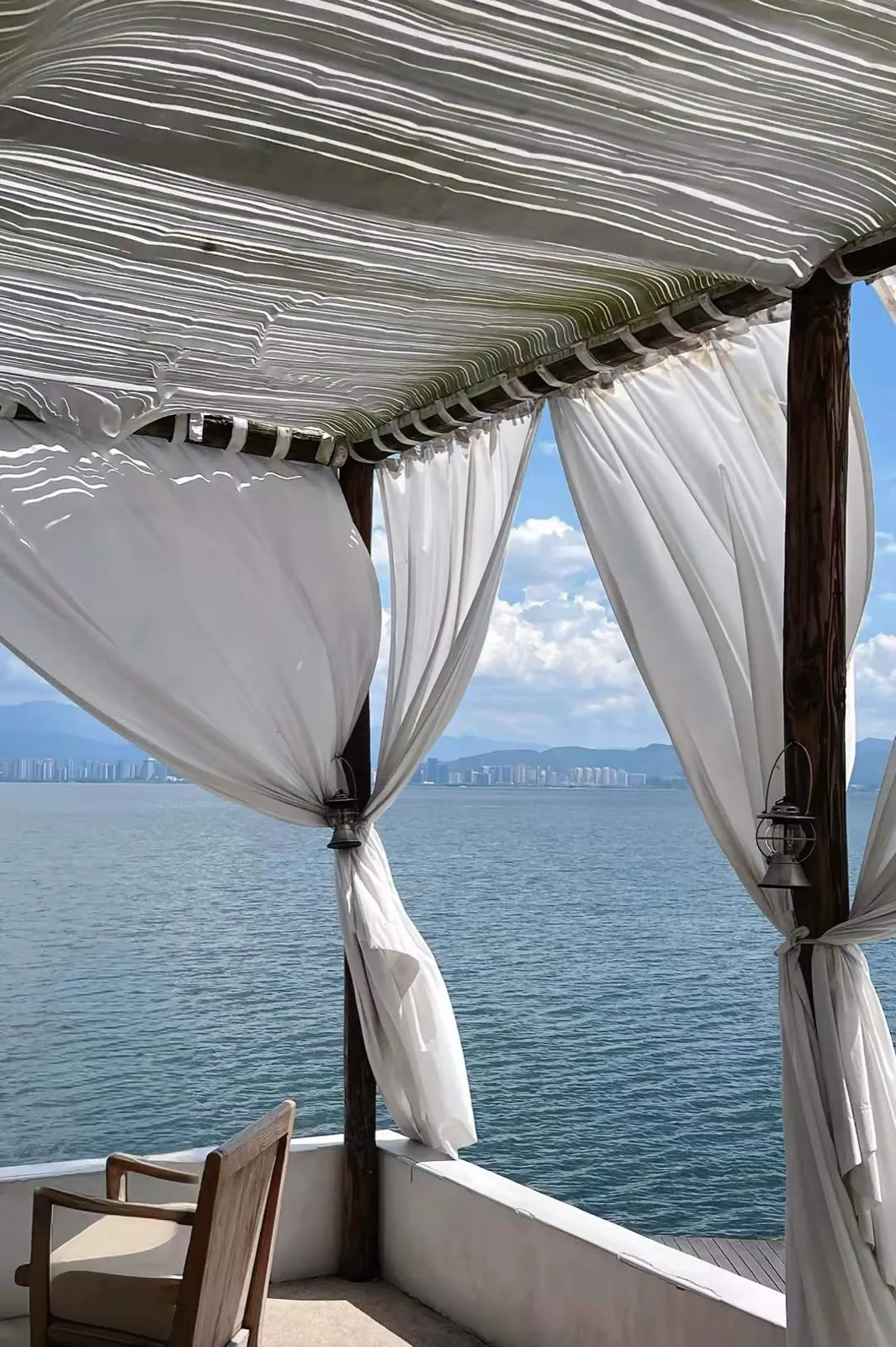 A cabana with white curtains over the sea.