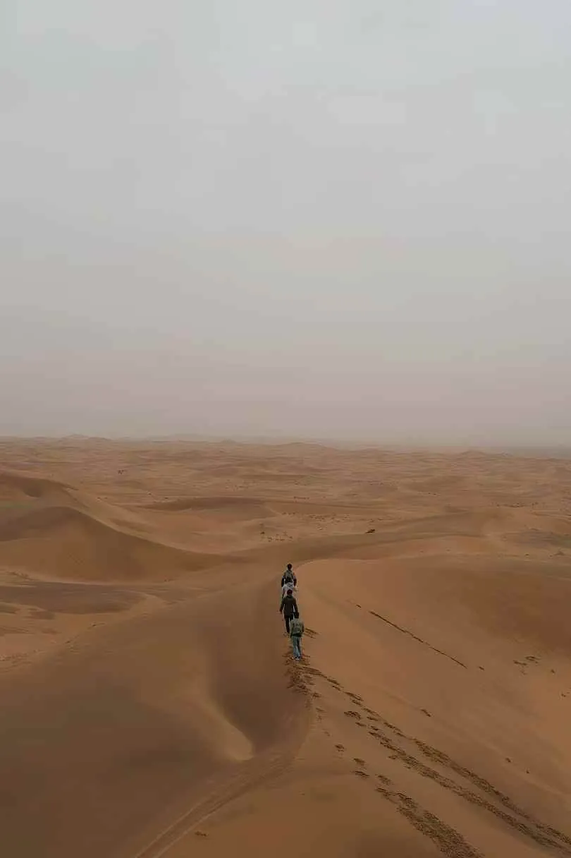 People walking in single file along a desert dune.