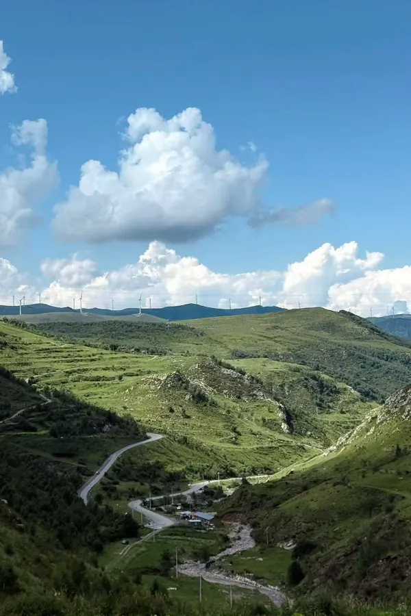 A green valley with a winding road under big summer clouds.