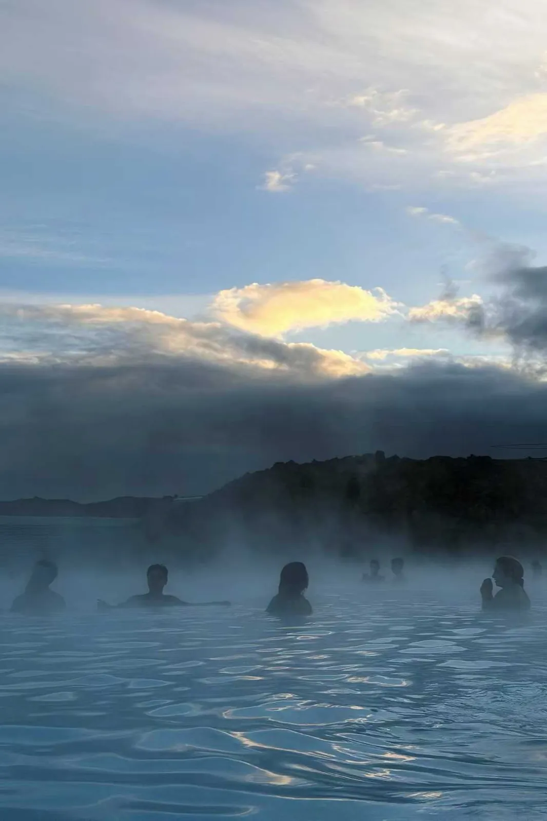 Bathers in a steaming geothermal lagoon under a low sky.