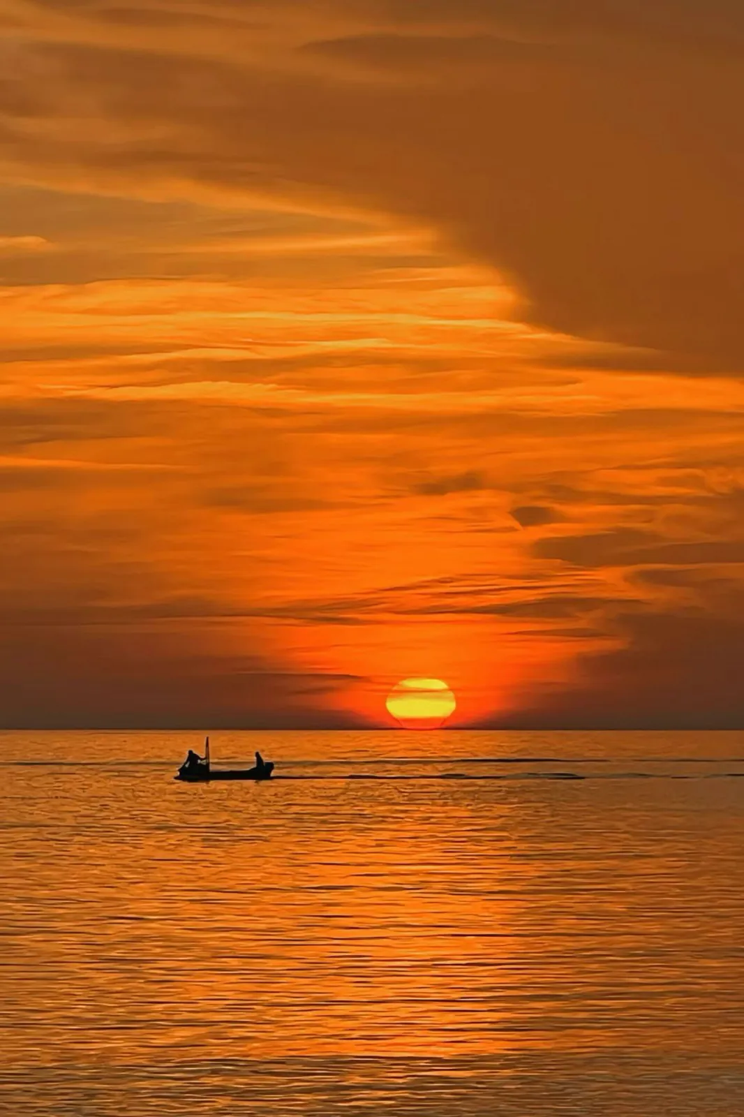 An orange sunset over the sea, a small boat below.