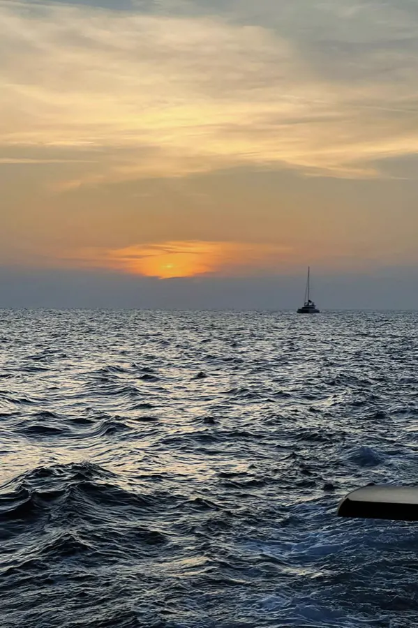 A sailboat on the sea under a low sunset.