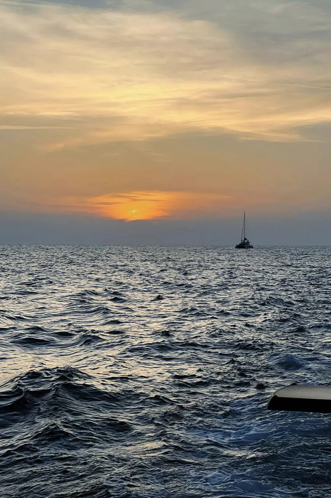 A sailboat on the sea under a low sunset.