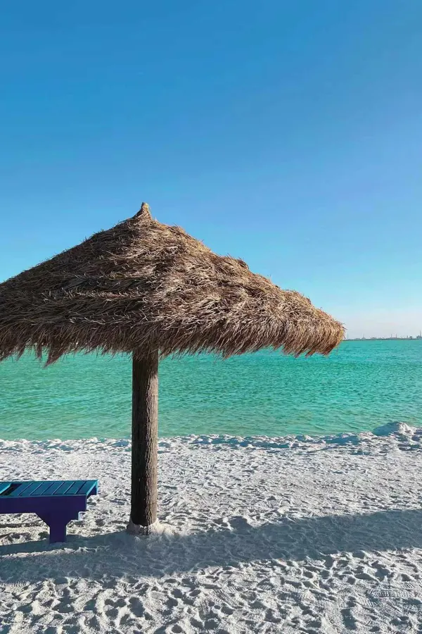 A straw umbrella on a white beach, turquoise sea behind.