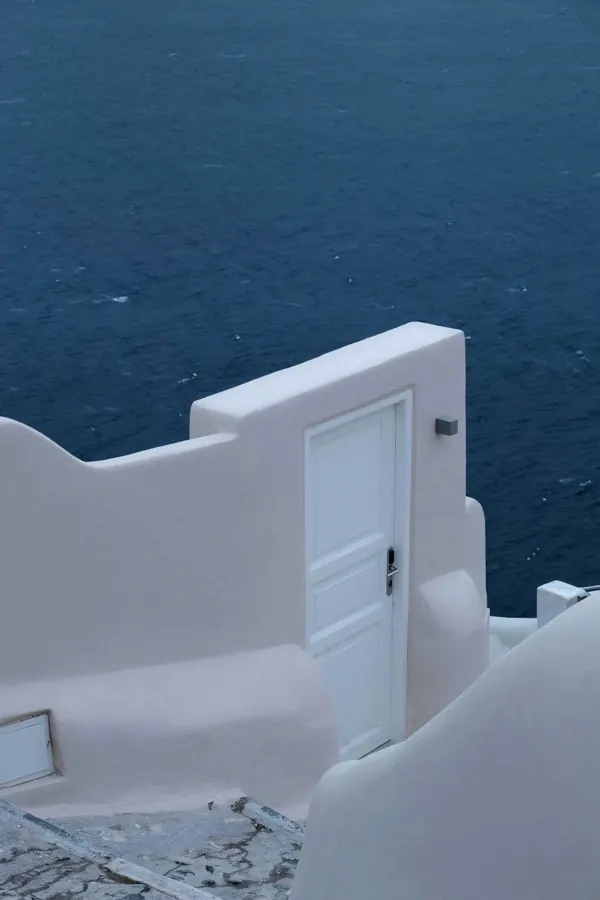 A white door on a whitewashed terrace above the sea.