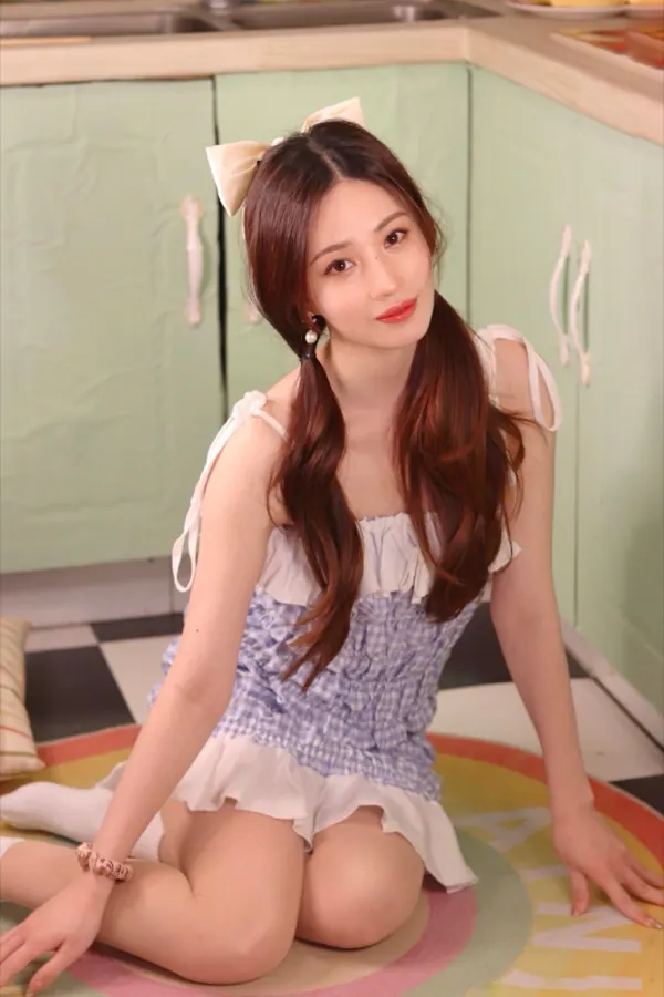 Sitting on a kitchen floor in a gingham dress, a white bow in the hair.