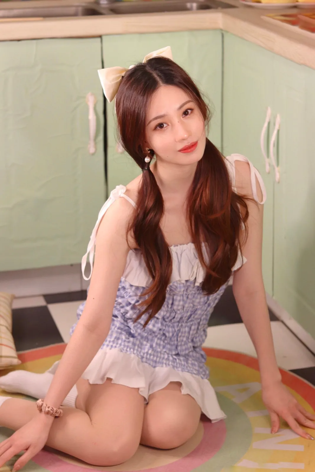 Sitting on a kitchen floor in a gingham dress, a white bow in the hair.