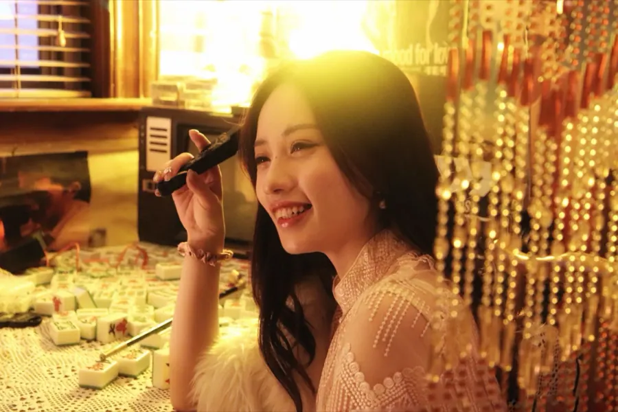 Laughing by a mahjong table and a curtain of gold beads.