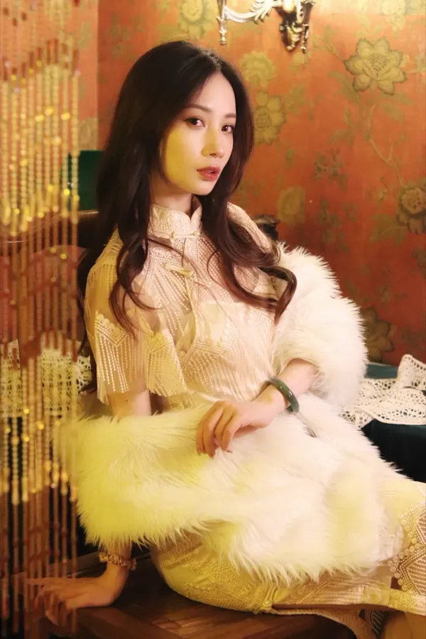 A cream lace qipao and a white fur stole, against floral wallpaper.