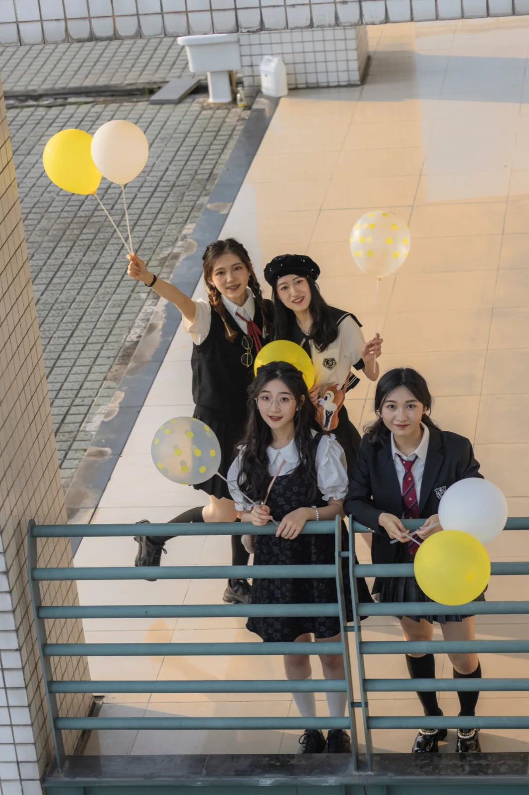 Four friends with yellow balloons, seen from above on a balcony.