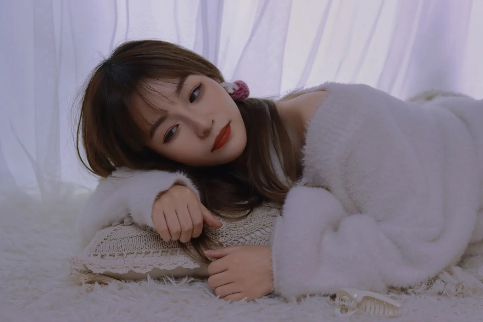 Lying on a white rug in a soft white sweater.