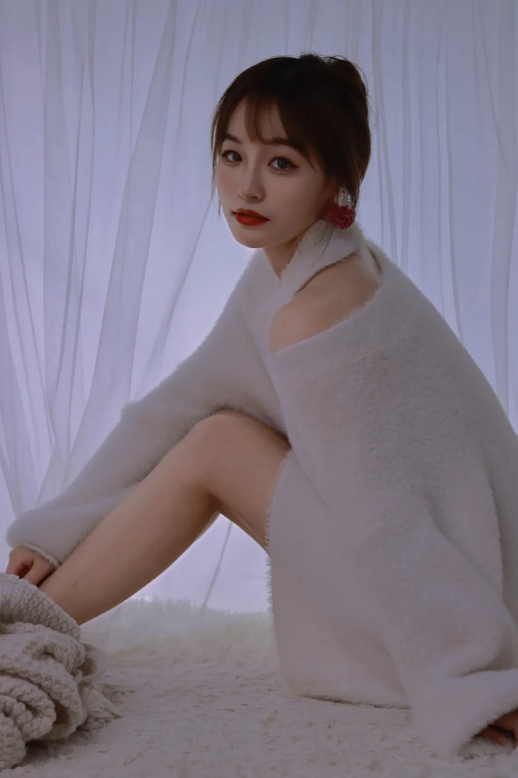 A white sweater before a sheer white curtain.