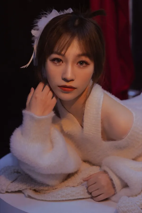 A white sweater in a dark room, a feather clip in the hair.