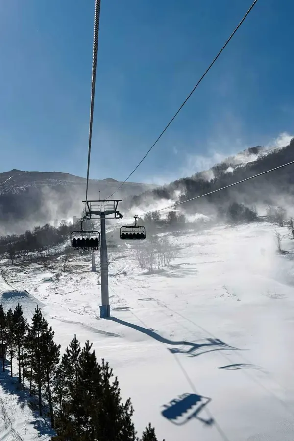 A chairlift climbing through blowing snow, its shadow on the piste.
