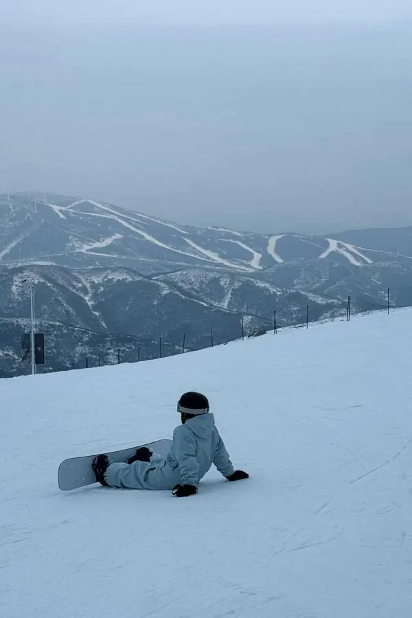 Sitting on the slope with the board, ski runs on the far ridge.