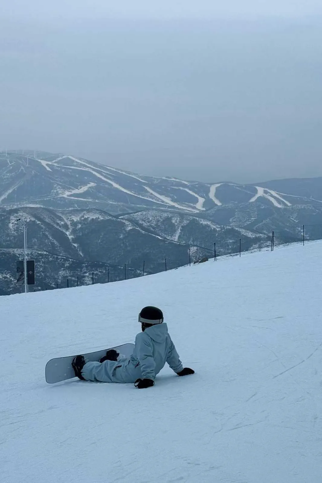 Sitting on the slope with the board, ski runs on the far ridge.