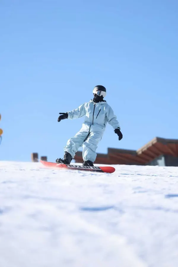 Riding a snowboard under a clear blue sky, shot low from the snow.