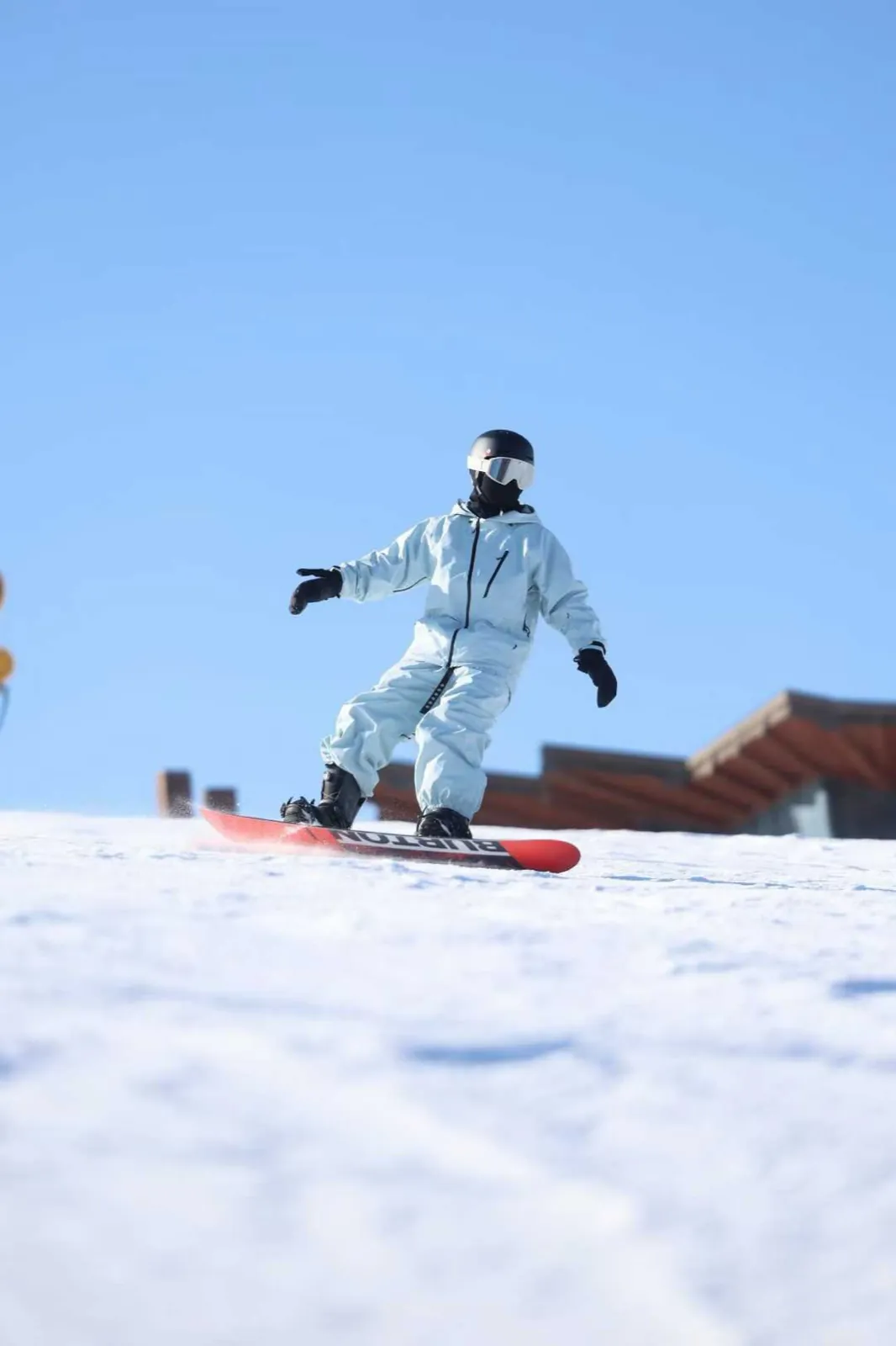 Riding a snowboard under a clear blue sky, shot low from the snow.