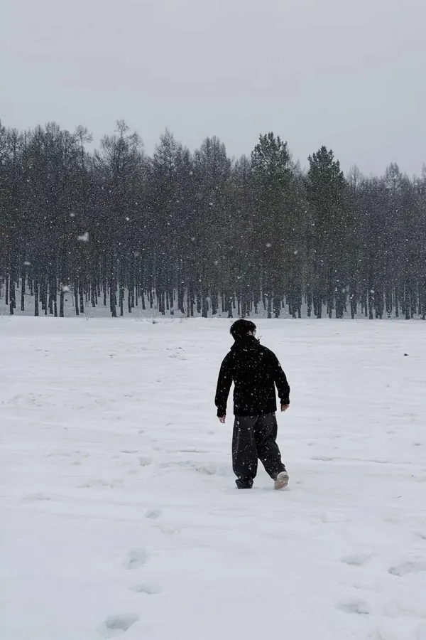 Walking across a snowfield towards the trees while it snows.