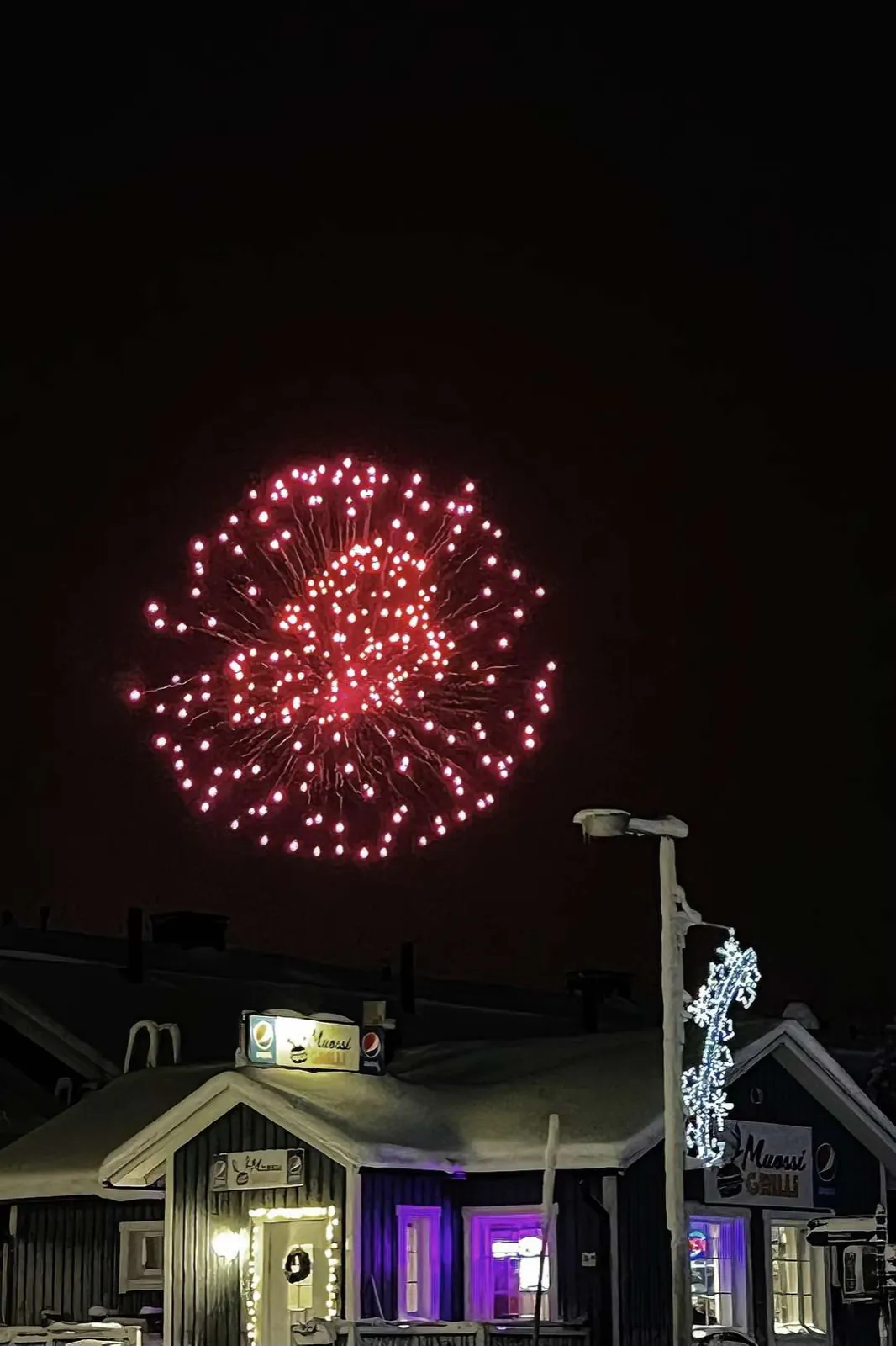 Red fireworks above a snowy village at night.