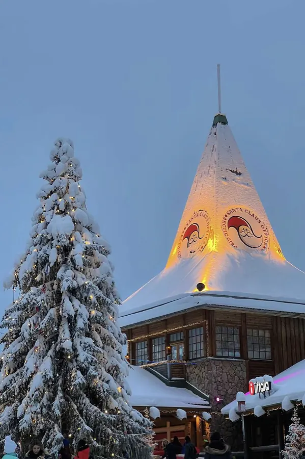 A snow-covered tree and a lit wooden house.